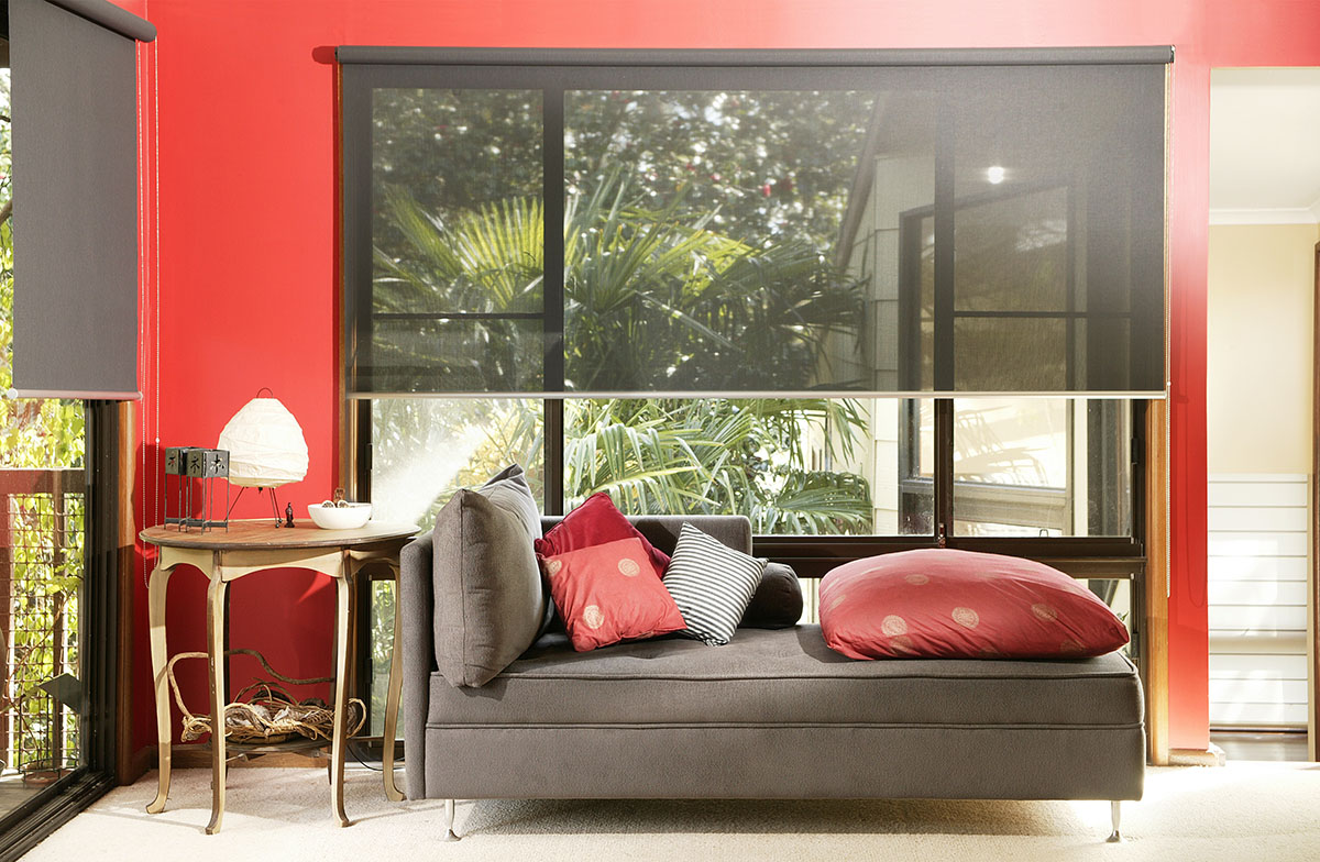 brown couch with red pillows and red walls with interior shades halfway down