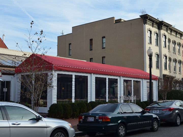 cars parked out front of a restaurant with red canopy and white roll down screens